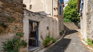 A narrow street with stone buildings, a blue door, and potted plants.