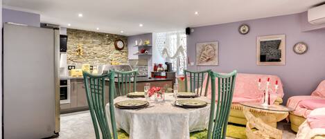 Una cocina moderna con salpicadero de pared de piedra, un comedor con mesa redonda y sillas, y una sala de estar con sofá y una pequeña mesita auxiliar.
