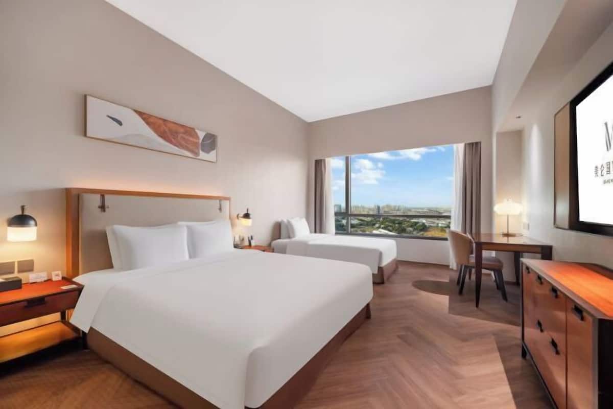 Ein Hotelzimmer mit einem großen Bett, zwei Einzelbetten, einem Schreibtisch und Blick auf die Stadt.