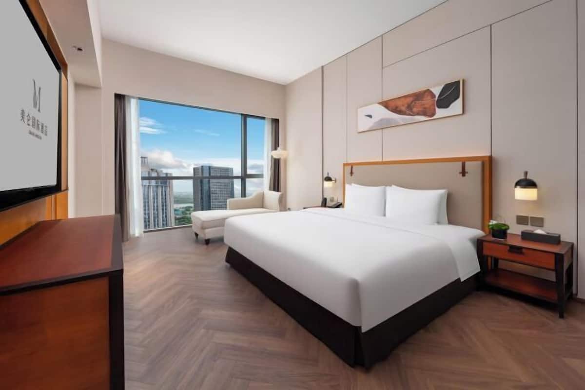 Ein modernes Hotelzimmer mit einem großen Bett, einem Schreibtisch, einem Stuhl und Blick auf die Stadt.