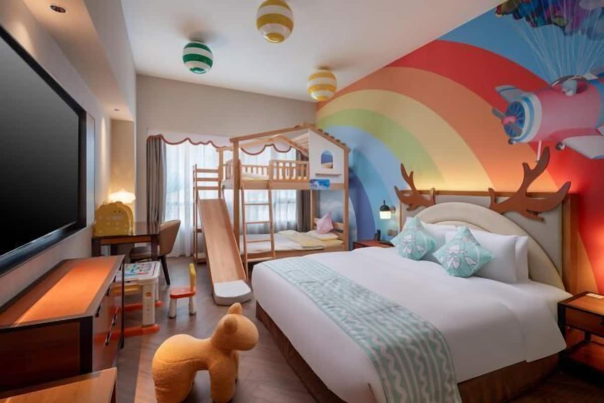 Kinderzimmer mit Etagenbetten, einer Rutsche, einem Fernseher und einer Wandmalerei einer Regenbogen und einer fliegenden Katze.
