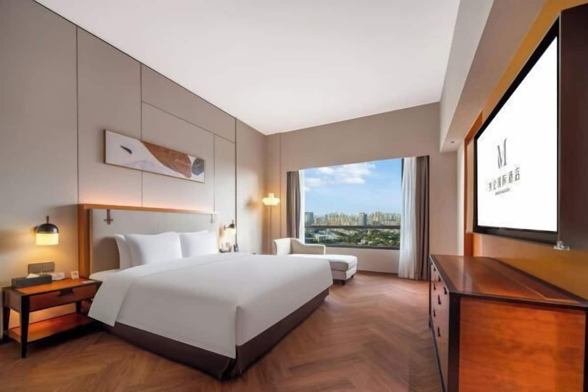 Ein modernes Hotelzimmer mit einem großen Bett, einem Schreibtisch und Blick auf die Stadt durch große Fenster.