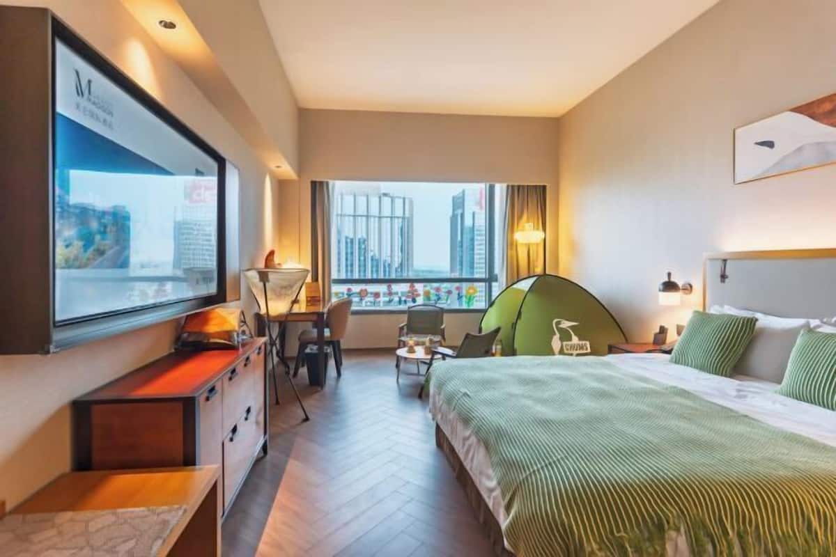 Ein Hotelzimmer mit Bett, Schreibtisch, Stuhl, Fernseher und einem Fenster mit Blick auf die Stadt.