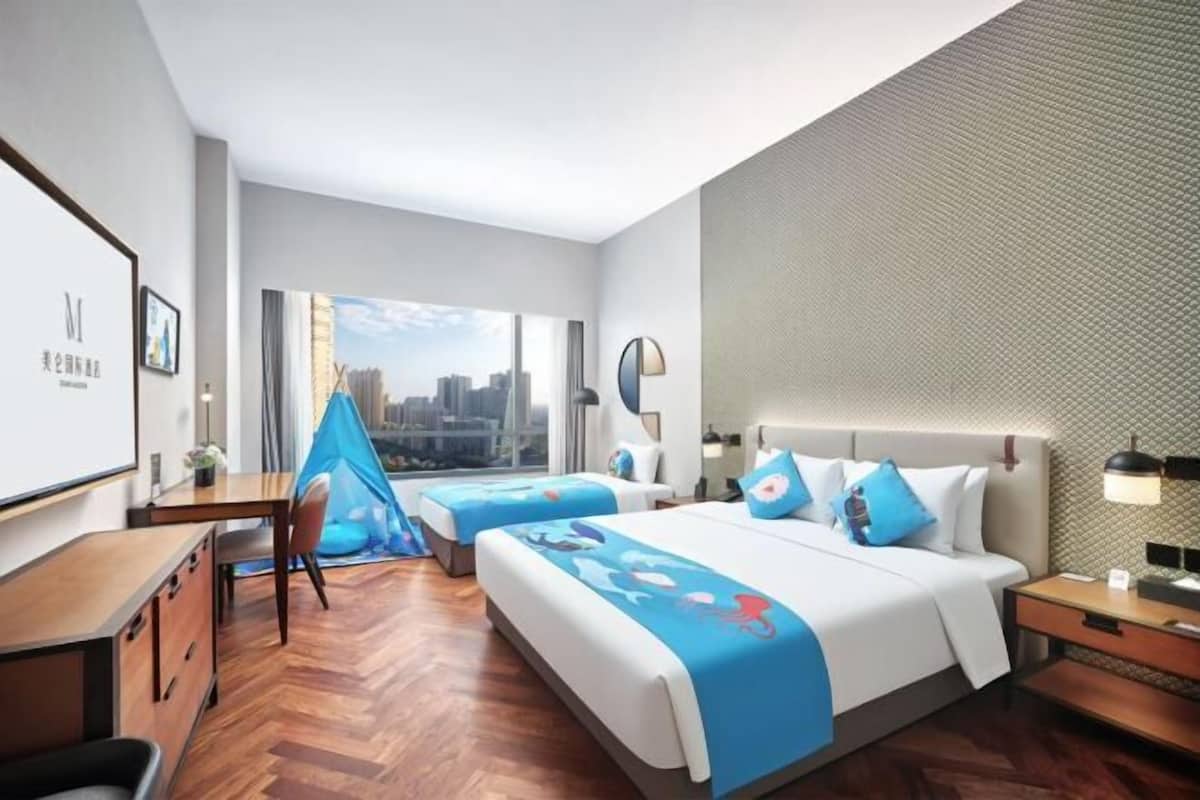 Ein Hotelzimmer mit Blick auf die Stadt, einem Schreibtisch, einem Sessel und einem Bett mit blauer Bettwäsche, sowie einem großen Fenster.