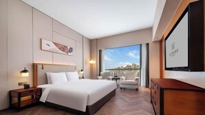 A modern hotel room with a large bed, a desk, a chair, a TV, and a view of the city. - Grand Madison Kunshan Huaqiao (Kunshan)