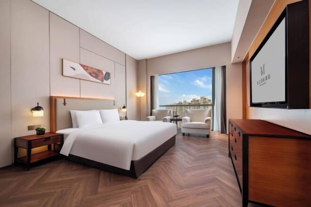 Ein modernes Hotelzimmer mit einem großen Bett, einem Schreibtisch, einem Stuhl, einem Fernseher und Blick auf die Stadt.