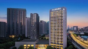 A high-rise hotel with a modern design, surrounded by other tall buildings and a well-lit parking area. - Grand Madison Kunshan Huaqiao (Kunshan)