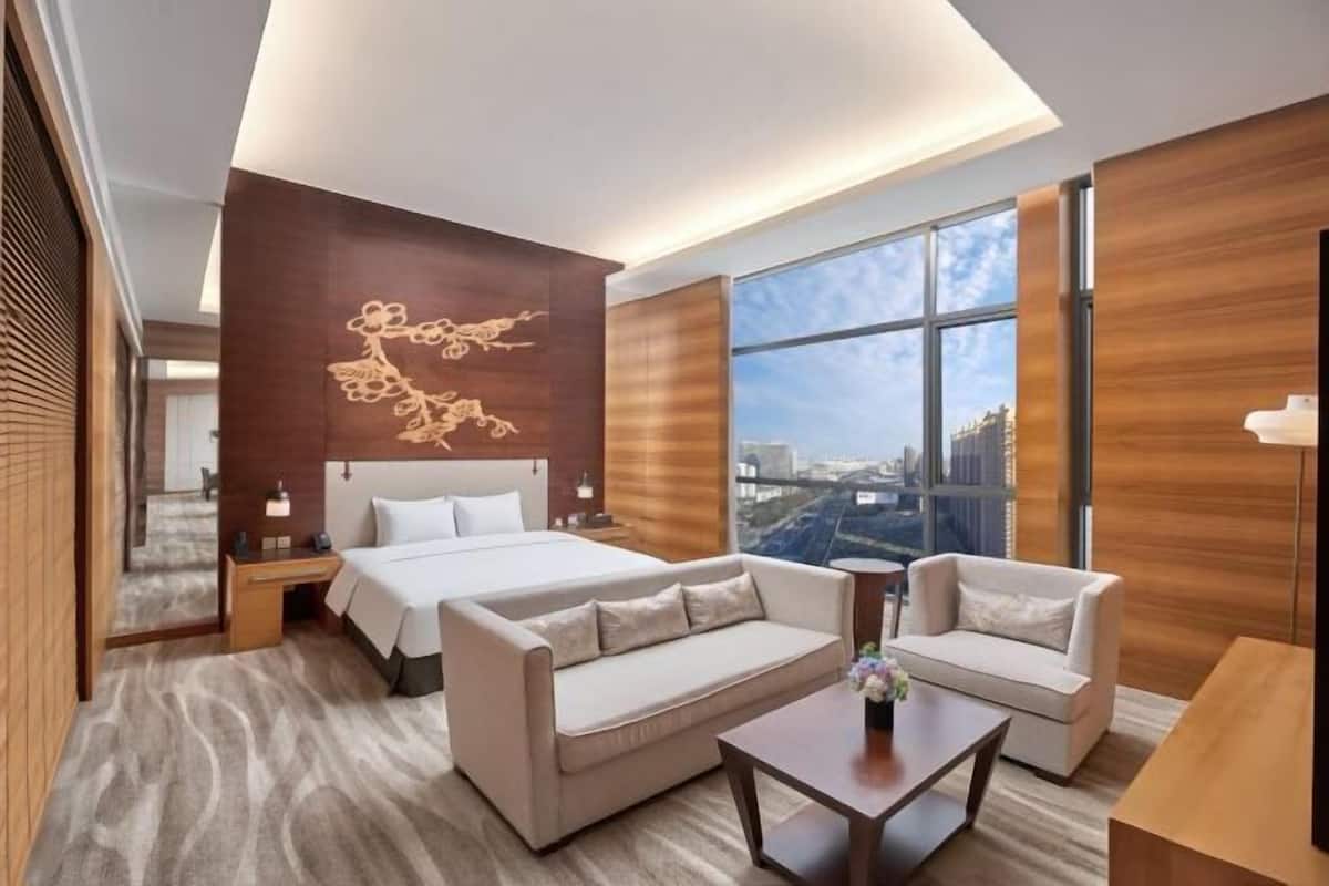 Ein Hotelzimmer mit einem Bett, zwei Sofas, einem kleinen Tisch und einem großen Fenster mit Blick auf die Stadt.