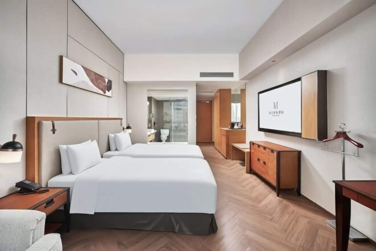 Ein modernes Hotelzimmer mit zwei Betten, einem Schreibtisch, einem Kleiderschrank und einem Fernseher.