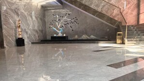 Un hall d’entrée spacieux doté d’un sol en marbre poli, d’une installation artistique en forme d’arbre et d’un escalier au design moderne.