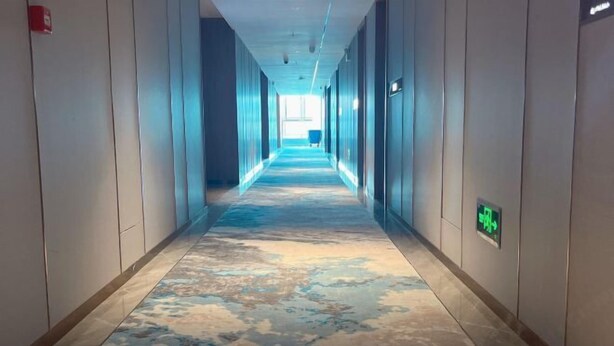 A long hallway with a patterned carpet, walls with a light color, and a visible exit sign. - Yincheng Holiday Hotel (Yongxing)