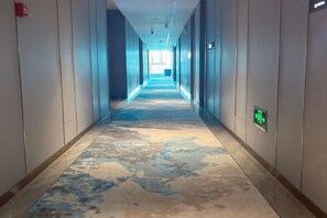 A long hallway with a patterned carpet, walls with a light color, and a visible exit sign. - Yincheng Holiday Hotel (Yongxing)