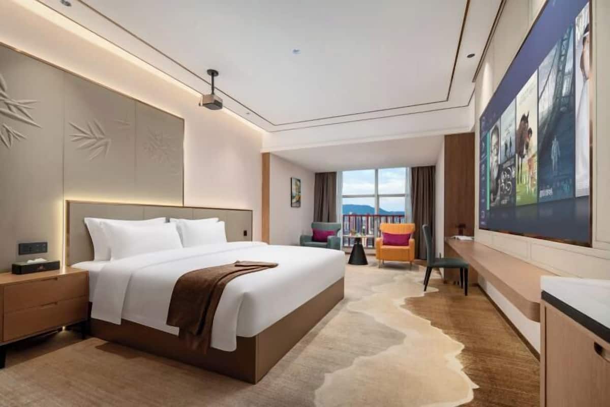 Een moderne hotelkamer met een groot bed, een bureau met stoel, een boekenkast en een groot raam met uitzicht.