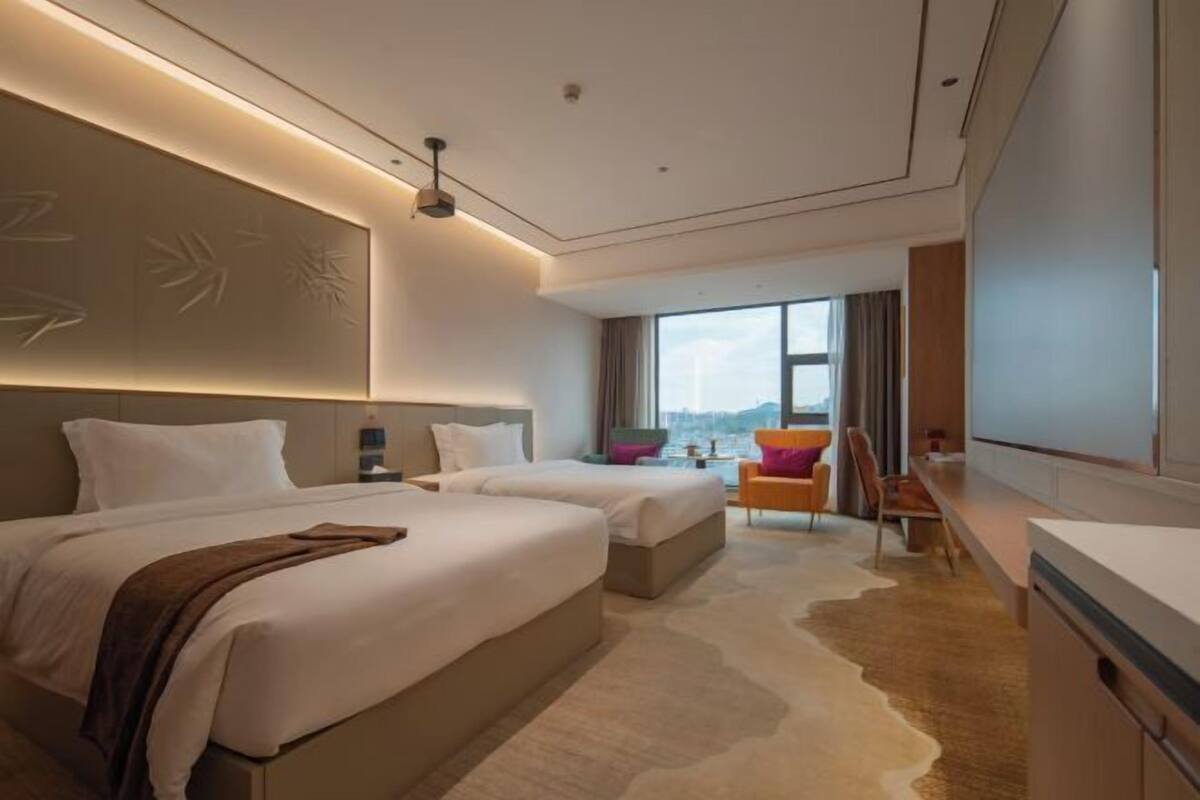 Een moderne hotelkamer met twee bedden, een groot raam, een bureau en uitzicht op de stad.