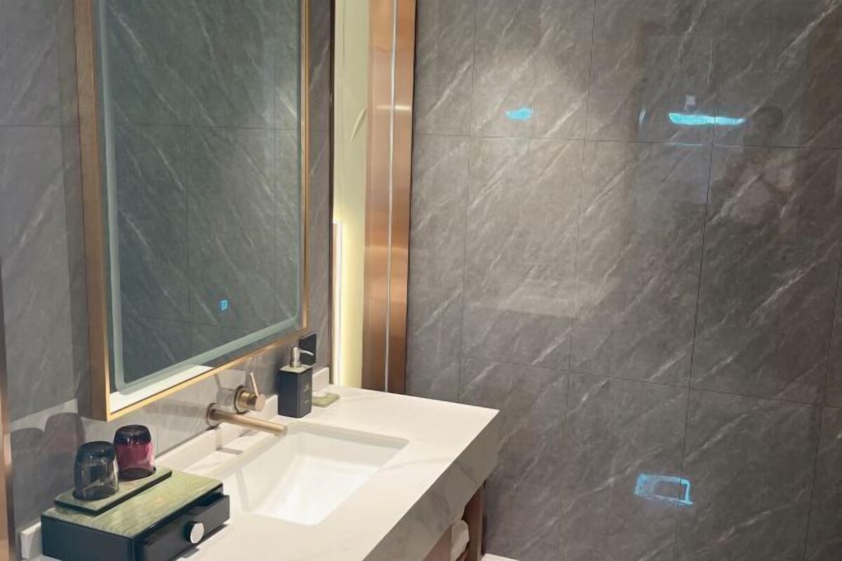 A modern bathroom with a large mirror, a white sink, and a marble wall.