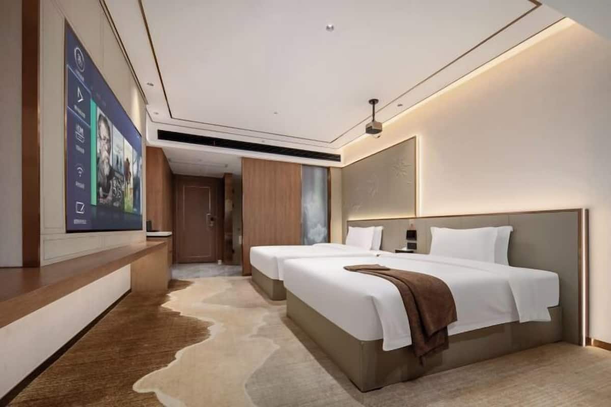Een moderne hotelkamer met twee bedden, een grote tv aan de wand en een houten accentmuur.