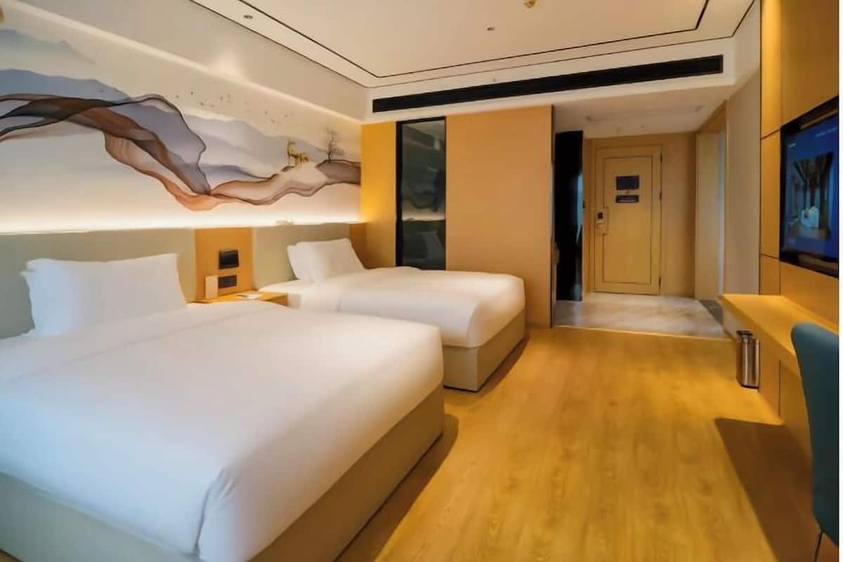 Een hotelkamer met twee bedden, een houten vloer, een muurschildering, een televisie en een deur.