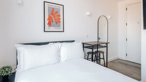 A modern bedroom with a bed, a desk, a chair, a mirror, and a framed artwork on the wall. - The Antigallican by Nestor (London)