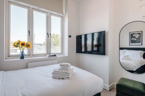 Quarto de hotel com cama, televisão, espelho e janela com girassóis.