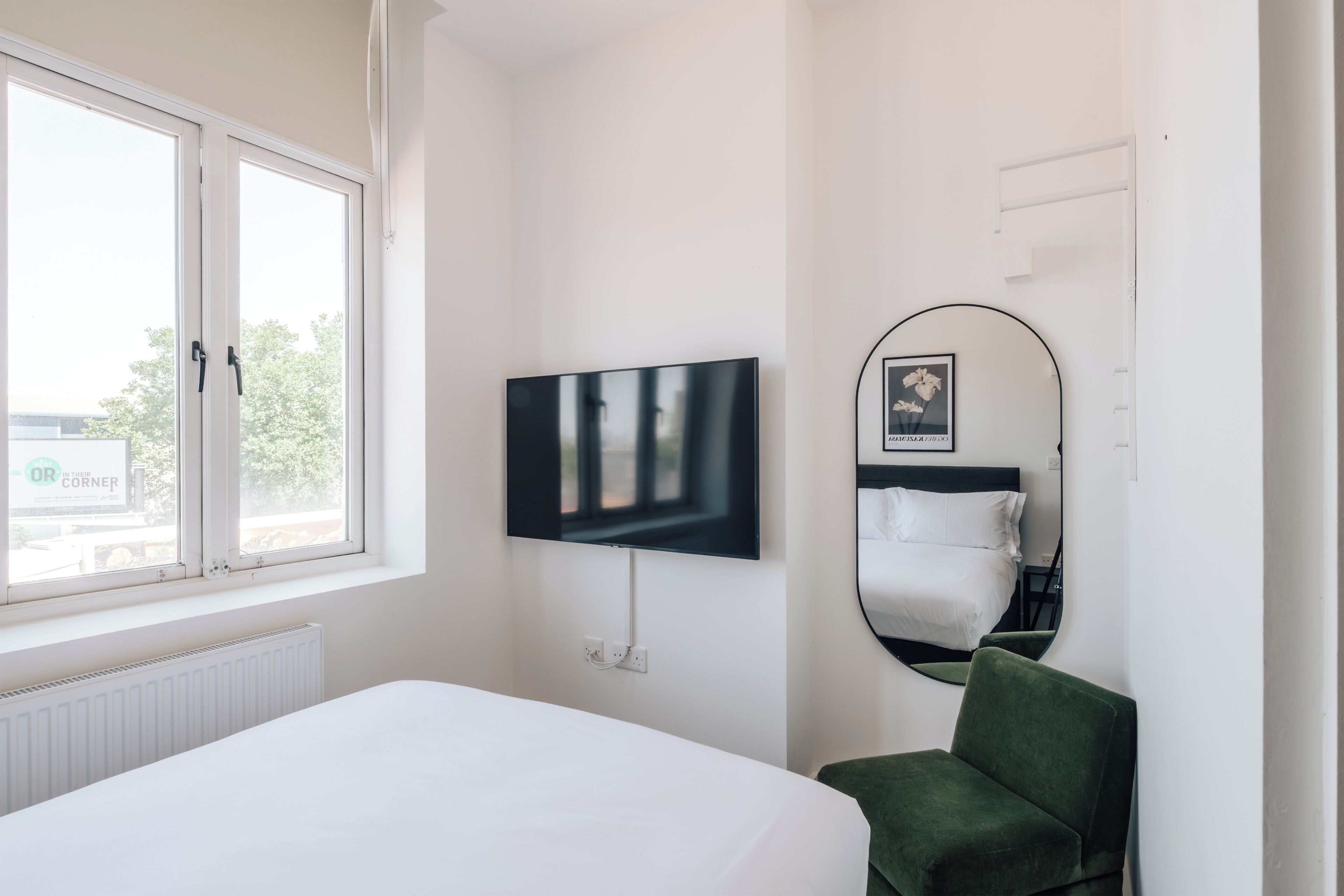 A hotel room with a bed, a television mounted on the wall, a window, and a mirror.