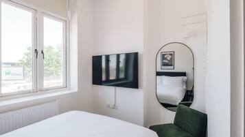 A hotel room with a bed, a television mounted on the wall, a window, and a mirror.