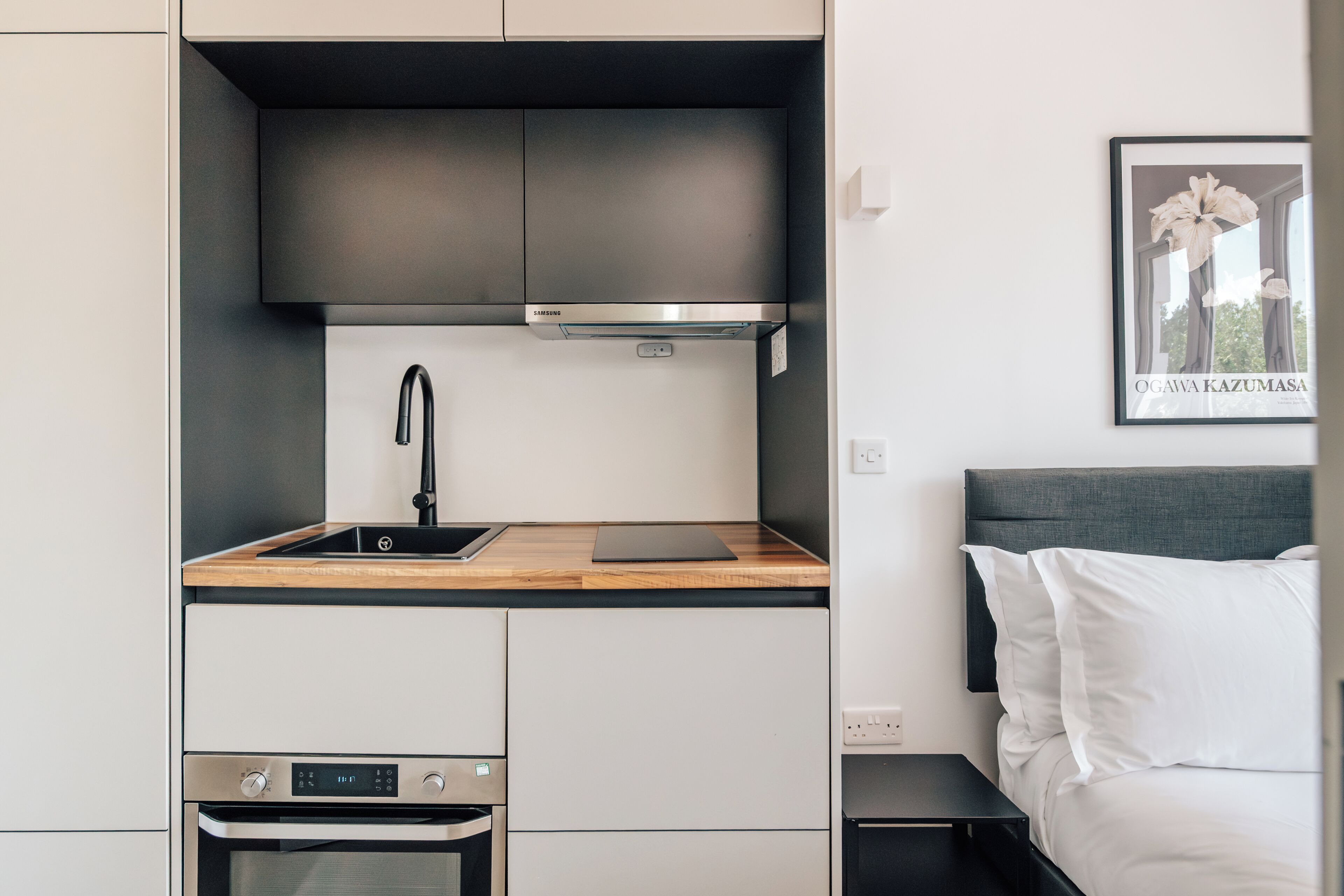 Una kitchenette compacta con horno de acero inoxidable, un lavamanos y un microondas.