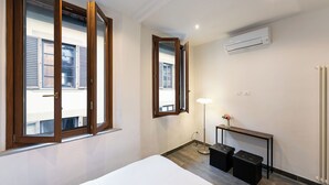 Hotellihuone, jossa on sänky, työpöytä, lamppu, peili ja ilmastointilaite.