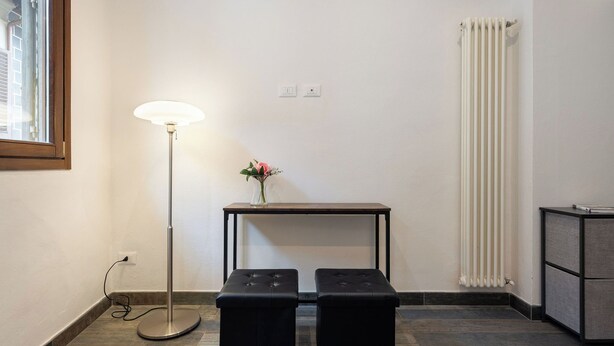 A room with a standing floor lamp, a small table with a vase, and two black ottomans.