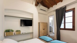 Quarto com cama, televisão na parede, roupeiro de madeira e janela com cortinas.