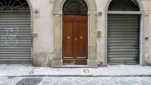 Um edifício com uma porta de madeira central, duas janelas em arco e um toldo de metal fechado à direita.