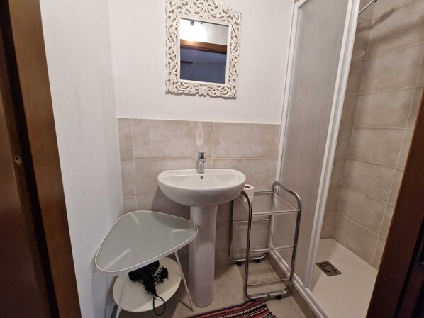 Un baño con lavamanos, espejo, ducha y toallero.