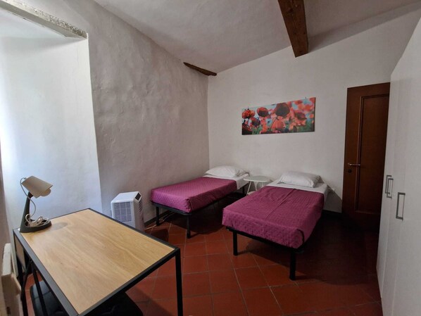 Una habitación con dos camas, una mesita, una silla, un calentador y una puerta.