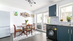 Une cuisine moderne équipée d’un lave-linge intégré, un coin repas avec une table ronde et des chaises, et une grande fenêtre laissant entrer la lumière naturelle.