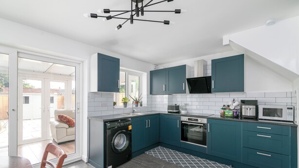 Une cuisine moderne avec des meubles de couleur turquoise, un lave-linge et un coin repas comprenant une table et des chaises.