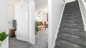 Un escalier dont les marches sont recouvertes de moquette, menant à un palier où se trouvent un banc et une plante.