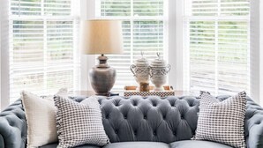 A room with a grey tufted sofa, a table with a lamp, and decorative items.
