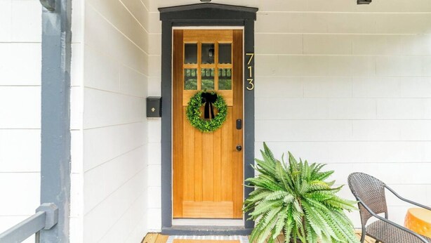 A wooden door with a wreath, a number '713' on the wall, and a potted plant beside a chair.