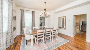 A dining area with a wooden table, white chairs, a chandelier, and a patterned rug.