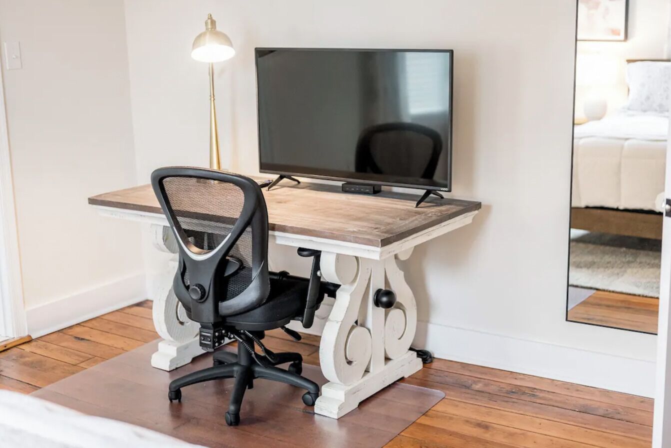 A modern office space with a wooden desk, black office chair, and a flat-screen TV.