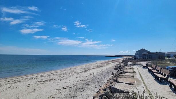 Une plage avec une clôture en bois, des bancs et une maison offrant une vue sur la mer.
