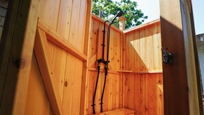 Une cabine de douche extérieure en bois, équipée de deux tuyaux et d’un pommeau de douche.