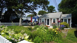 Un quartier résidentiel où l’on trouve des maisons dotées d’un porche à l’avant, d’une clôture en piquets et d’une variété de plantes à fleurs.