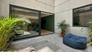 Un espacio exterior moderno con un ventanal que da a una habitación, un sillón de saco azul y plantas en macetas.