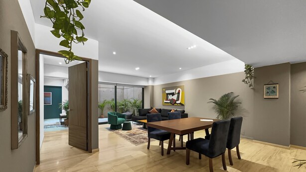 Una sala de estar moderna con una mesa de comedor de madera, sofás oscuros y un amplio ventanal.