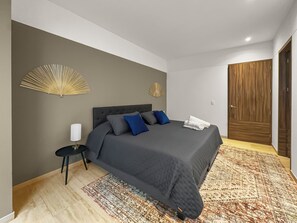 Une chambre moderne avec un grand lit, une petite table de chevet, un ventilateur décoratif fixé au mur et une porte en bois.