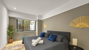 Un dormitorio moderno con una cama grande, una planta en maceta, una ventana y un adorno de pared.
