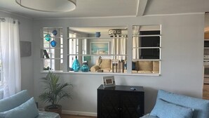 A living room with a sofa, a black cabinet, and a large mirror. - Enjoy views of beautiful Houghton Lake in charming LARGE home that sleeps 10.  (Houghton Lake)