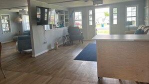 A spacious living area with a wooden floor, a blue sofa, a white coffee table, and a TV mounted on the wall. - Enjoy views of beautiful Houghton Lake in charming LARGE home that sleeps 10.  (Houghton Lake)