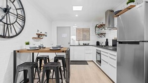 A compact kitchen with a central island, stainless steel appliances, and a large clock on the wall. - 2 Cute by Experience Jervis Bay (Huskisson)