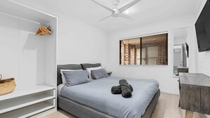 A modern bedroom with a bed, a wardrobe, a television, and a window with blinds. - 2 Cute by Experience Jervis Bay (Huskisson)
